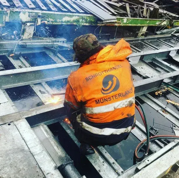 Mitarbeiter in Schrotthandel-Münsterland-Jacke zerlegt Metallschrott mit dem Schneidbrenner
