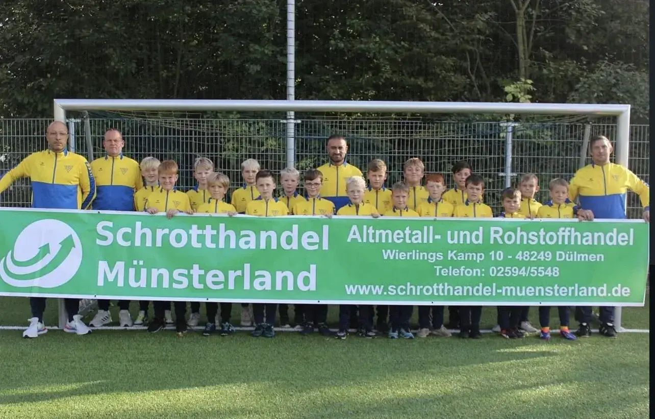 Jugendmannschaft mit Trainern hinter einem Banner von Schrotthandel Münsterland auf dem Fußballplatz